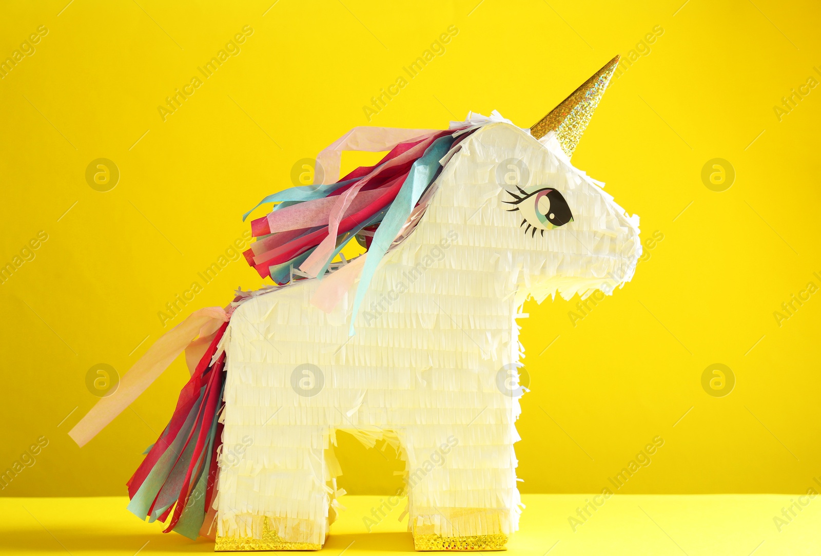 Photo of Bright pinata in shape of unicorn on yellow background