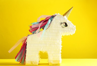 Photo of Bright pinata in shape of unicorn on yellow background