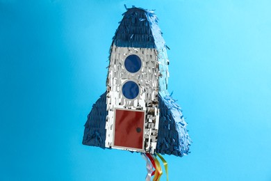 Photo of Bright pinata in shape of spaceship hanging on light blue background