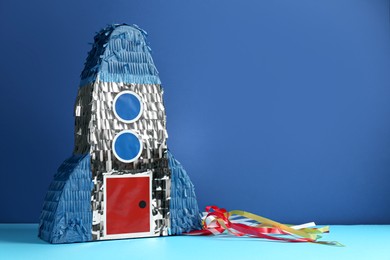 Photo of Bright pinata in shape of spaceship on blue background. Space for text