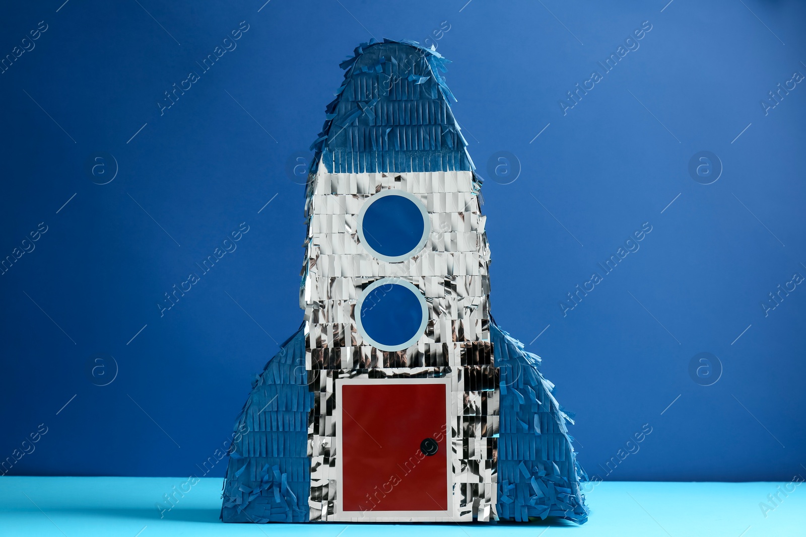 Photo of Bright pinata in shape of spaceship on blue background