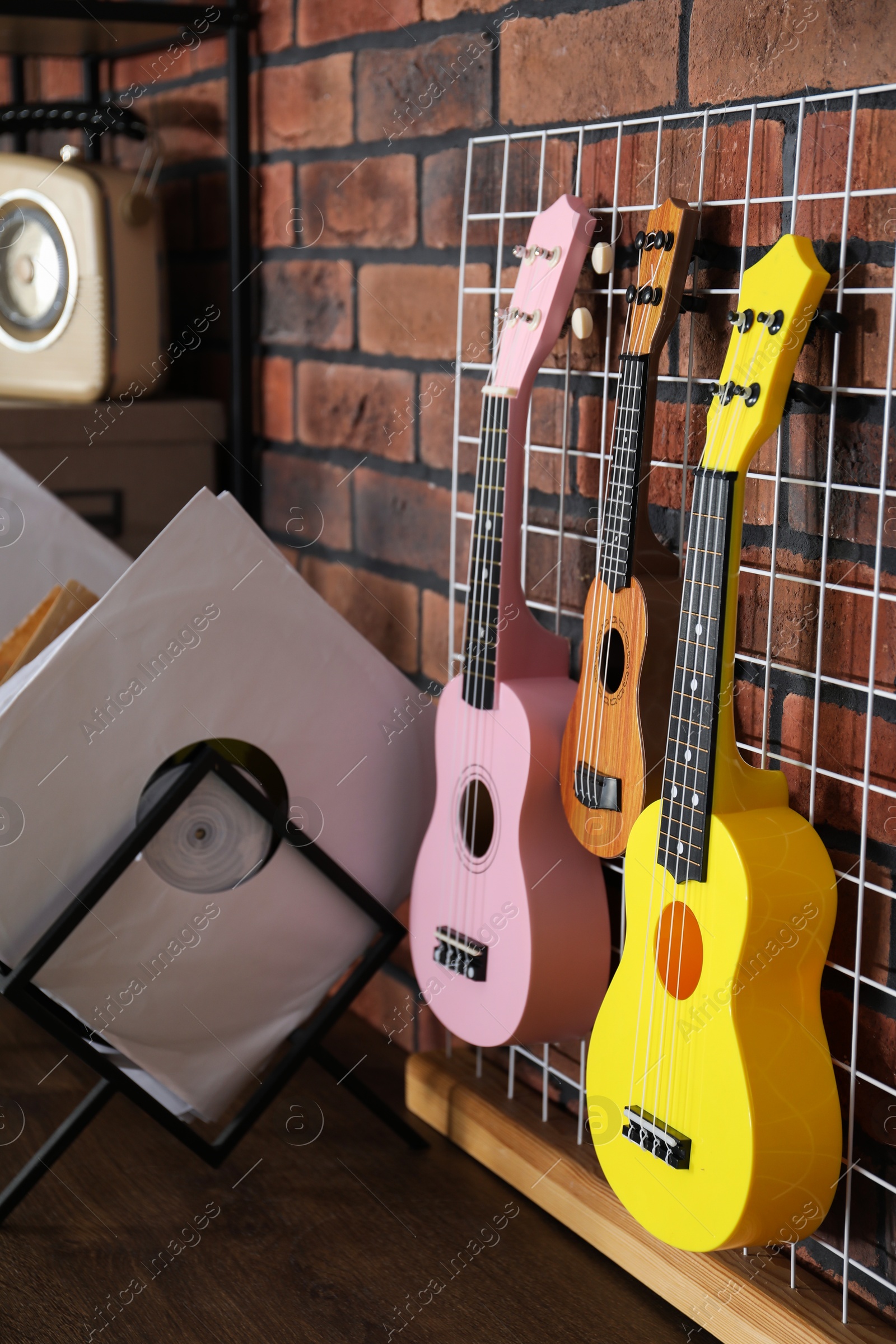 Photo of Three colorful ukulele on brick wall and records indoors