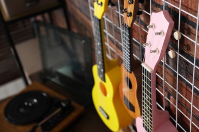 Photo of Three colorful ukulele on brick wall and record player indoors, closeup