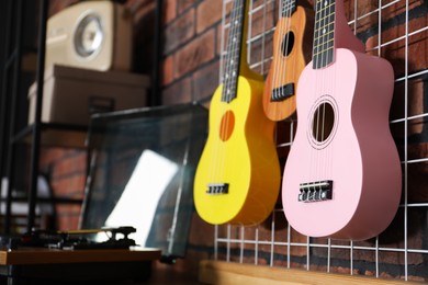 Photo of Three colorful ukulele on brick wall and record player indoors, closeup