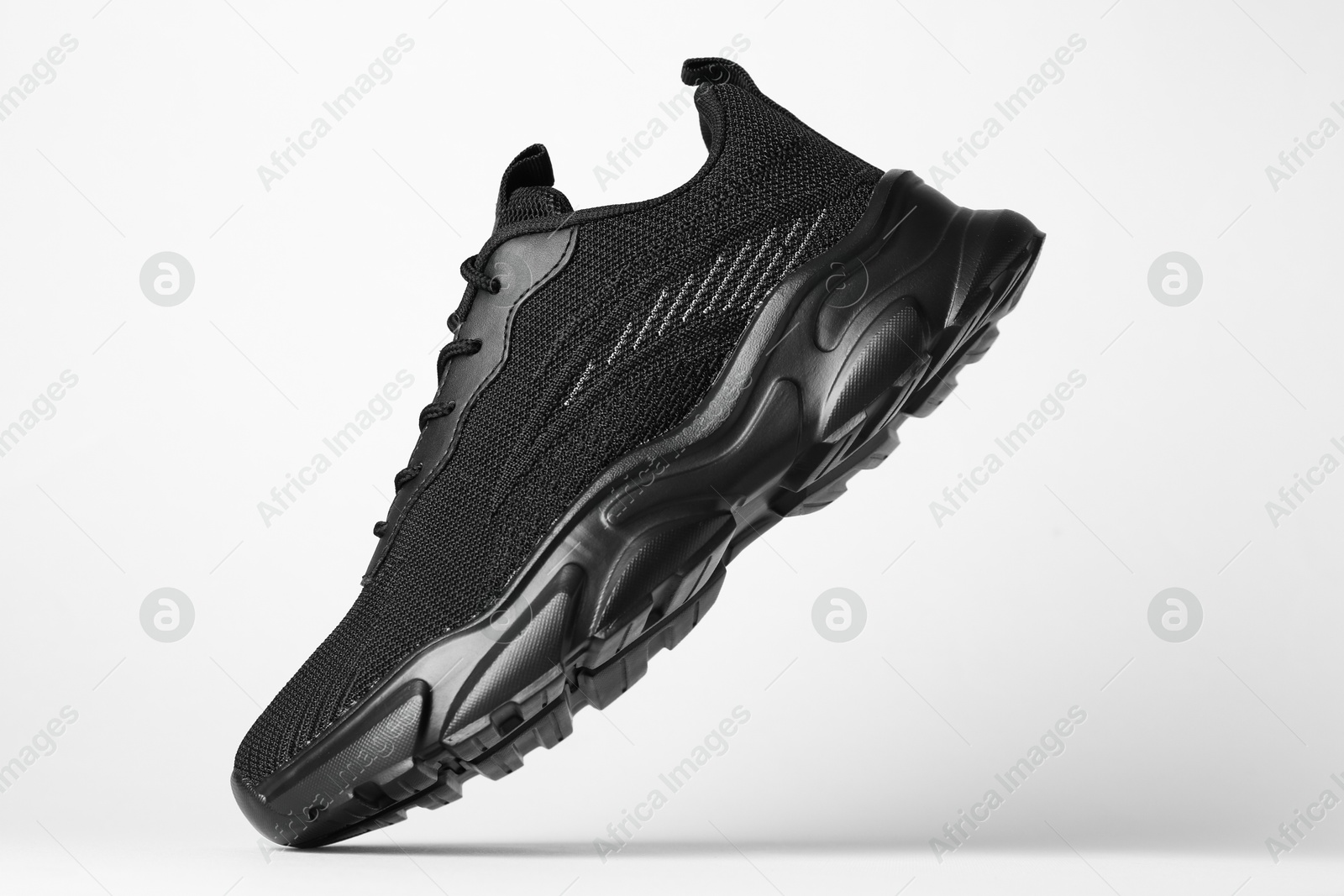 Photo of Stylish black sneaker in air against white background