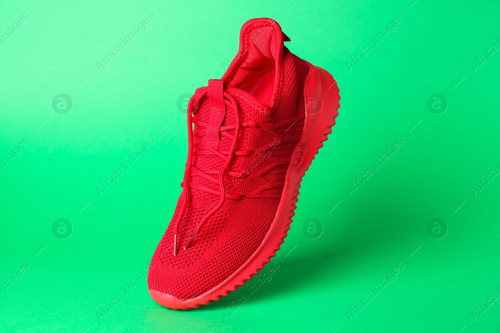 Photo of Stylish red sneaker in air against green background