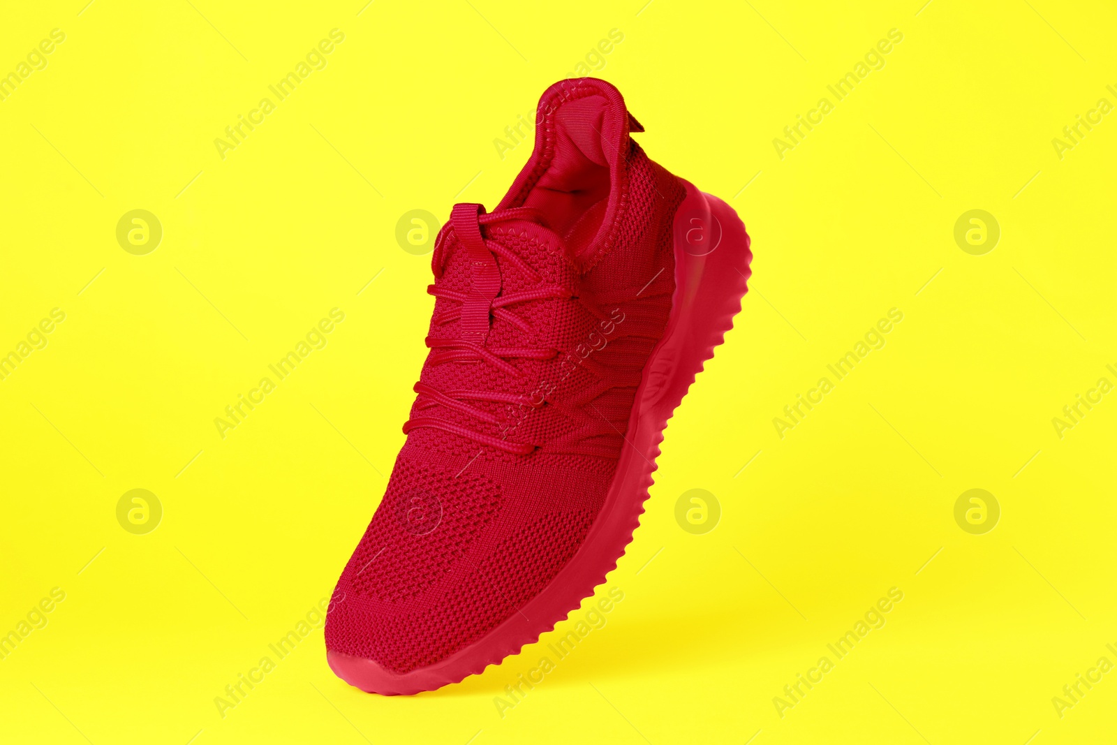 Photo of Stylish red sneaker in air against yellow background