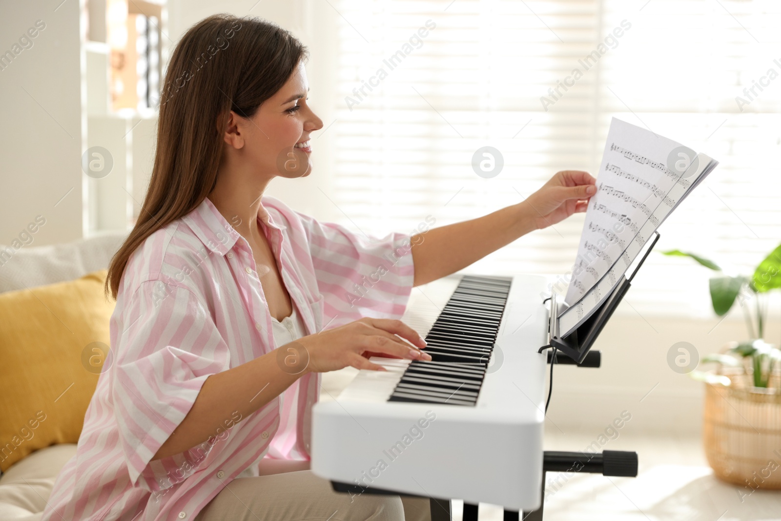 Photo of Smiling woman playing synthesizer at home. Electronic musical instrument