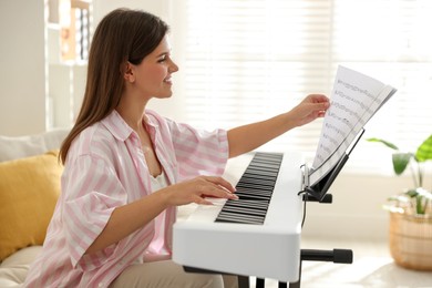 Smiling woman playing synthesizer at home. Electronic musical instrument