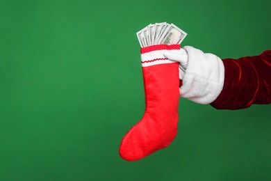 Photo of Santa Claus holding stocking with dollar banknotes on green background, closeup. Space for text