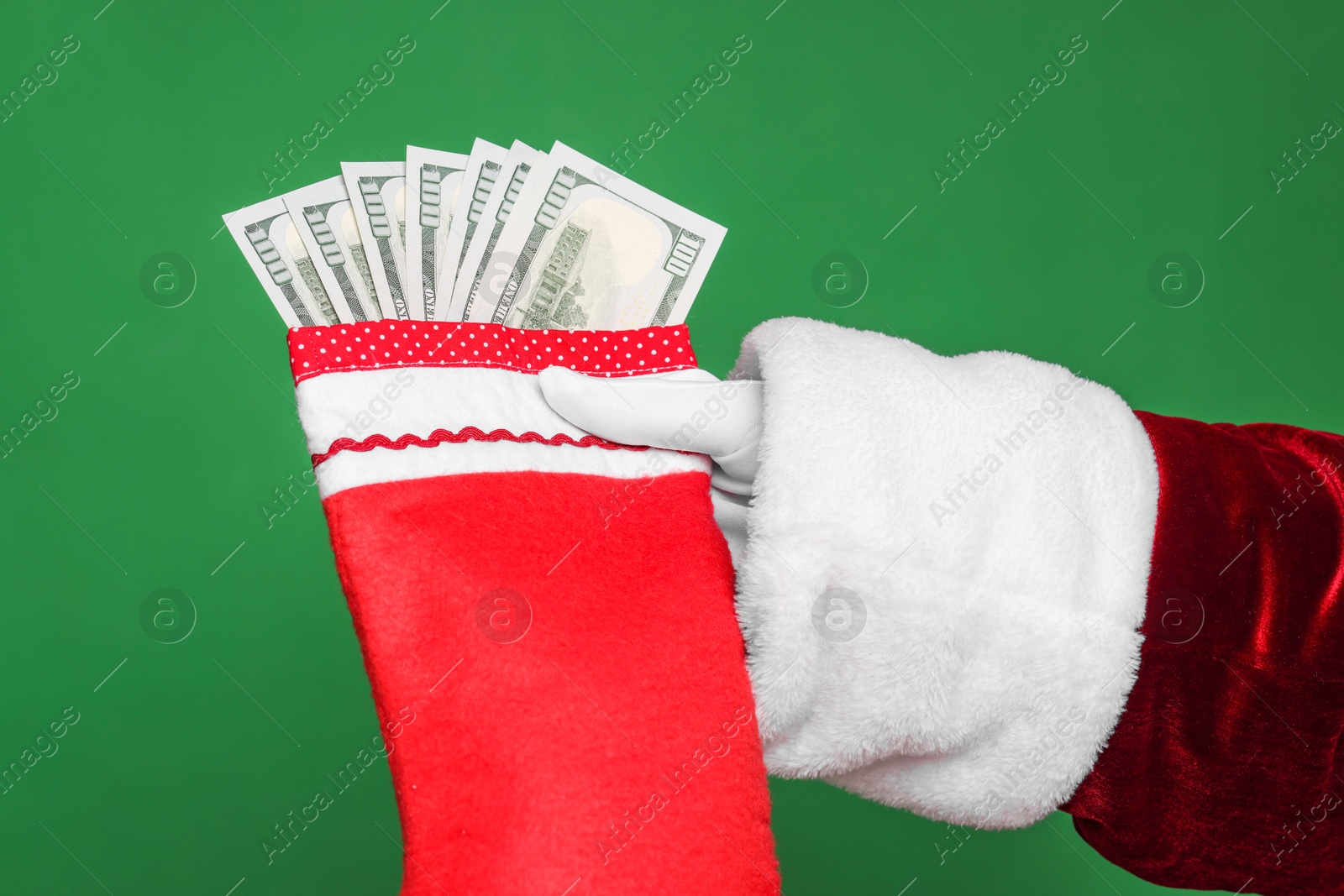 Photo of Santa Claus holding stocking with dollar banknotes on green background, closeup