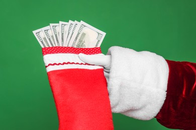 Photo of Santa Claus holding stocking with dollar banknotes on green background, closeup