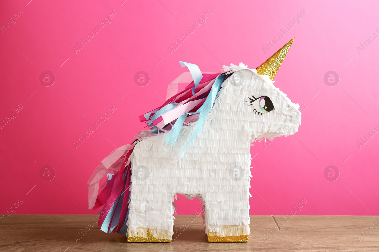 Photo of Beautiful pinata in shape of unicorn on wooden table against pink background