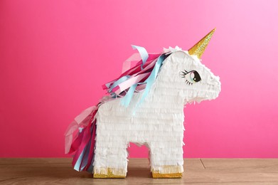 Photo of Beautiful pinata in shape of unicorn on wooden table against pink background