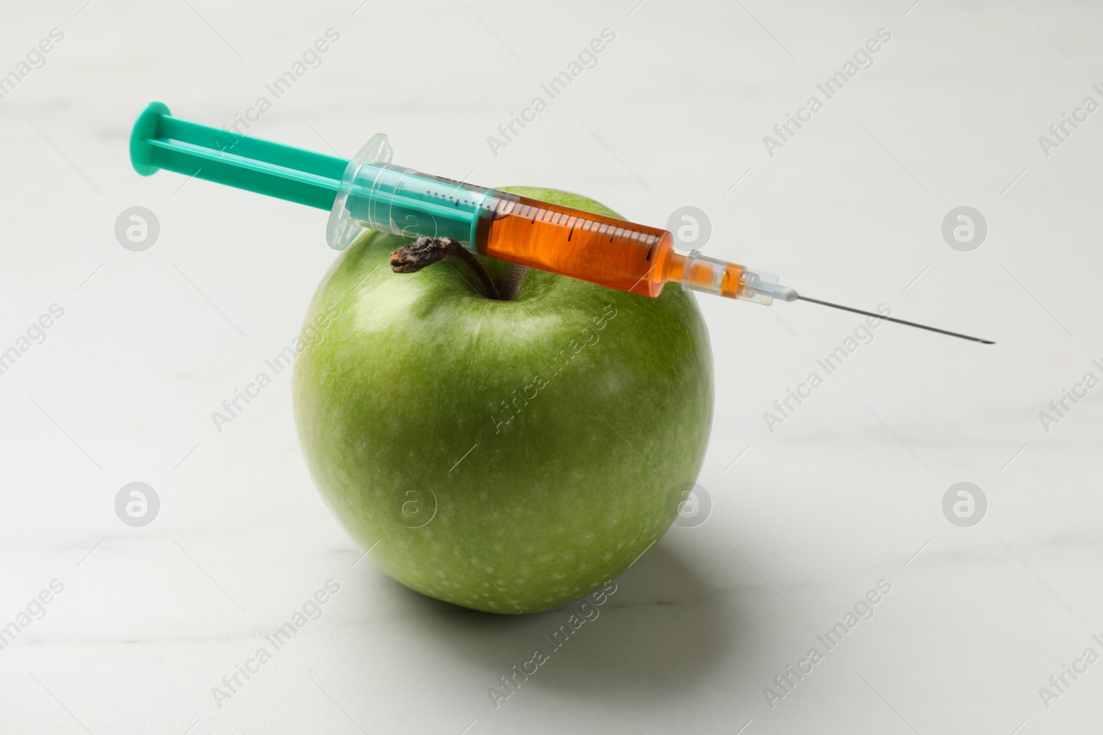 Photo of GMO concept. Green apple and syringe on white marble table, closeup