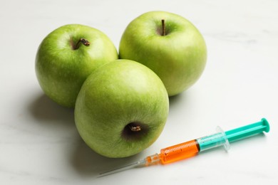 Photo of GMO concept. Green apples and syringe on white marble table, closeup