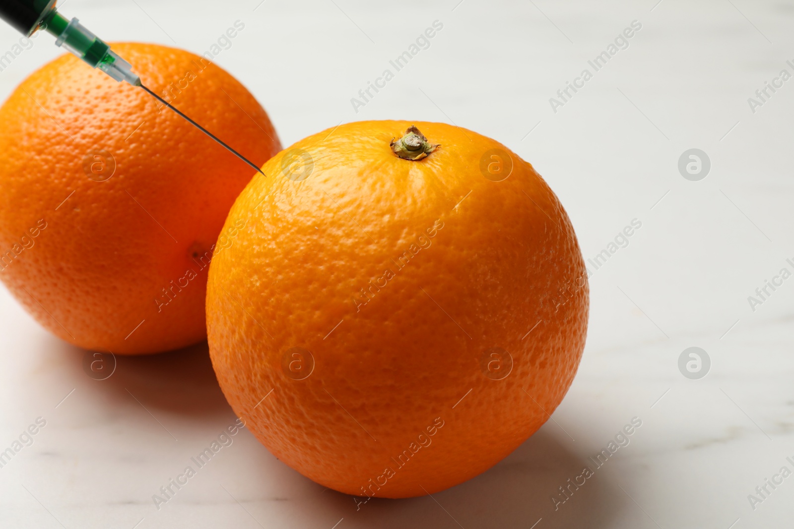 Photo of GMO concept. Injecting orange with syringe at white marble table, closeup