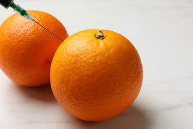 Photo of GMO concept. Injecting orange with syringe at white marble table, closeup