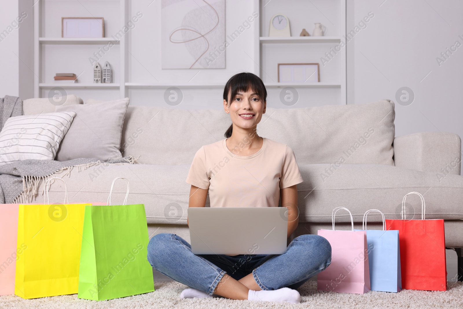 Photo of Internet shopping. Happy woman with laptop and colorful bags at home