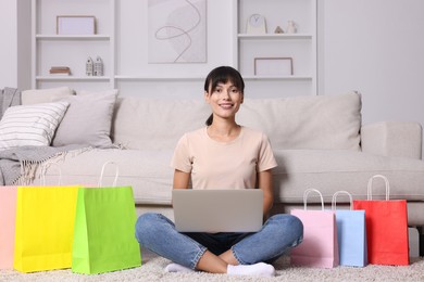 Photo of Internet shopping. Happy woman with laptop and colorful bags at home