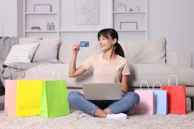 Photo of Internet shopping. Happy woman with credit card, laptop and colorful bags at home