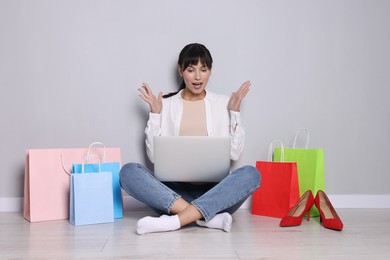 Photo of Internet shopping. Surprised woman with laptop and colorful bags sitting near grey wall