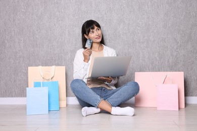 Photo of Internet shopping. Happy woman with credit card, laptop and colorful bags sitting near grey wall