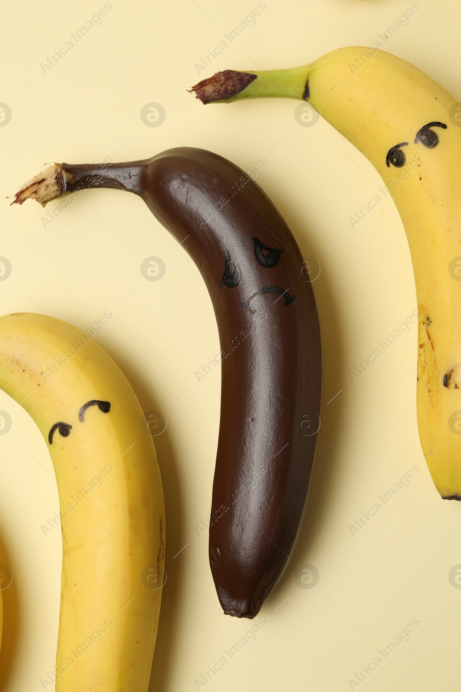 Photo of Stop racism. One dark banana among yellow ones on beige background, flat lay