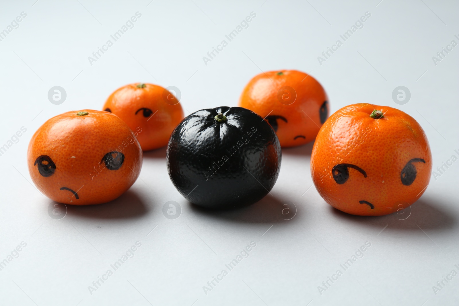 Photo of Stop racism. One black tangerine among orange ones on light background, closeup