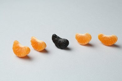 Photo of Stop racism. Black tangerine piece among orange ones on light background