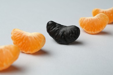 Photo of Stop racism. Black tangerine piece among orange ones on light background, closeup