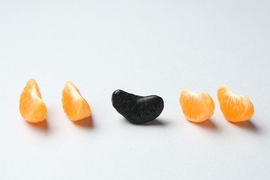 Photo of Stop racism. Black tangerine piece among orange ones on light background