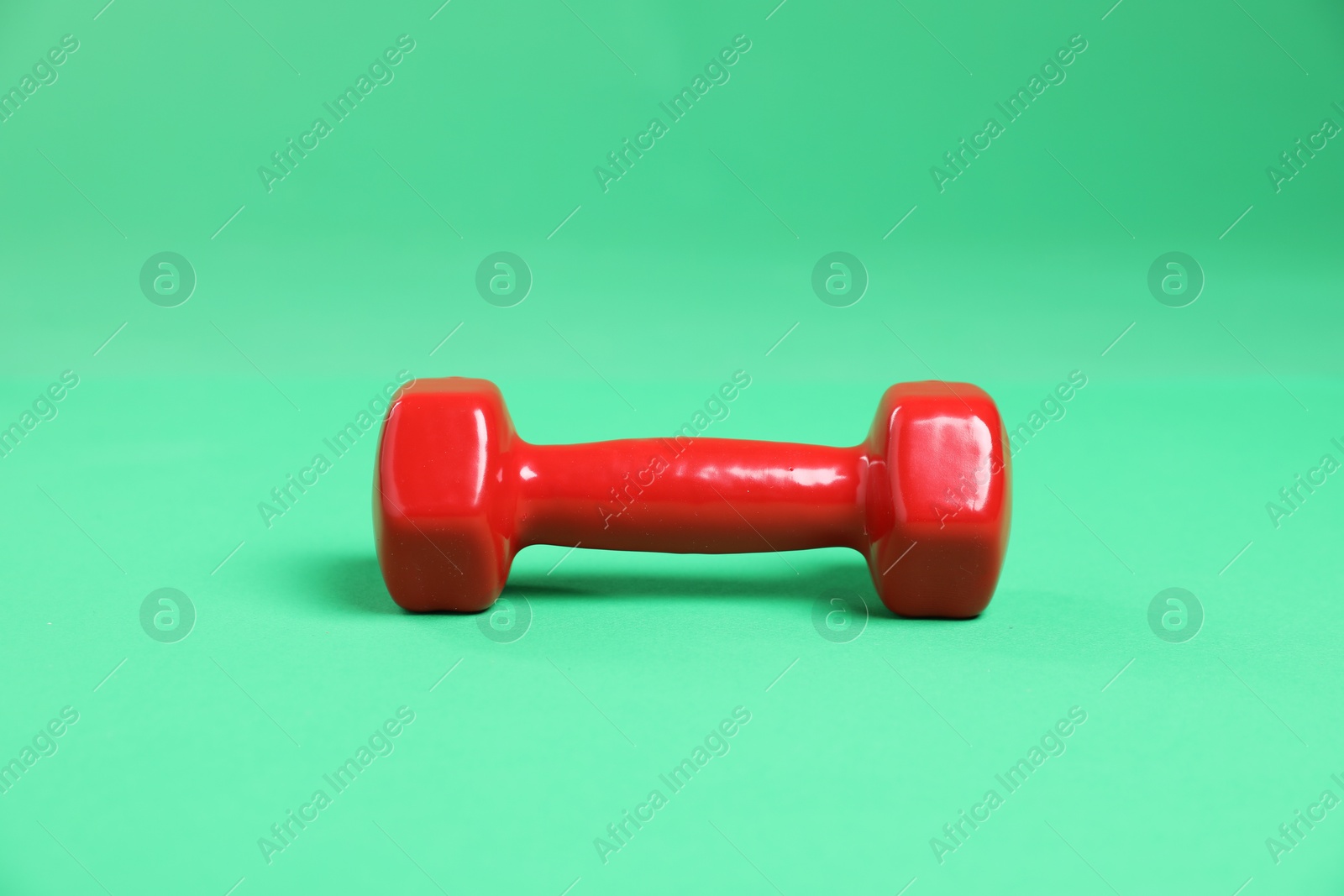 Photo of One red dumbbell on green background. Sports equipment