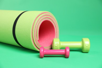 Photo of Fitness mat and dumbbells on green background, closeup. Sports equipment