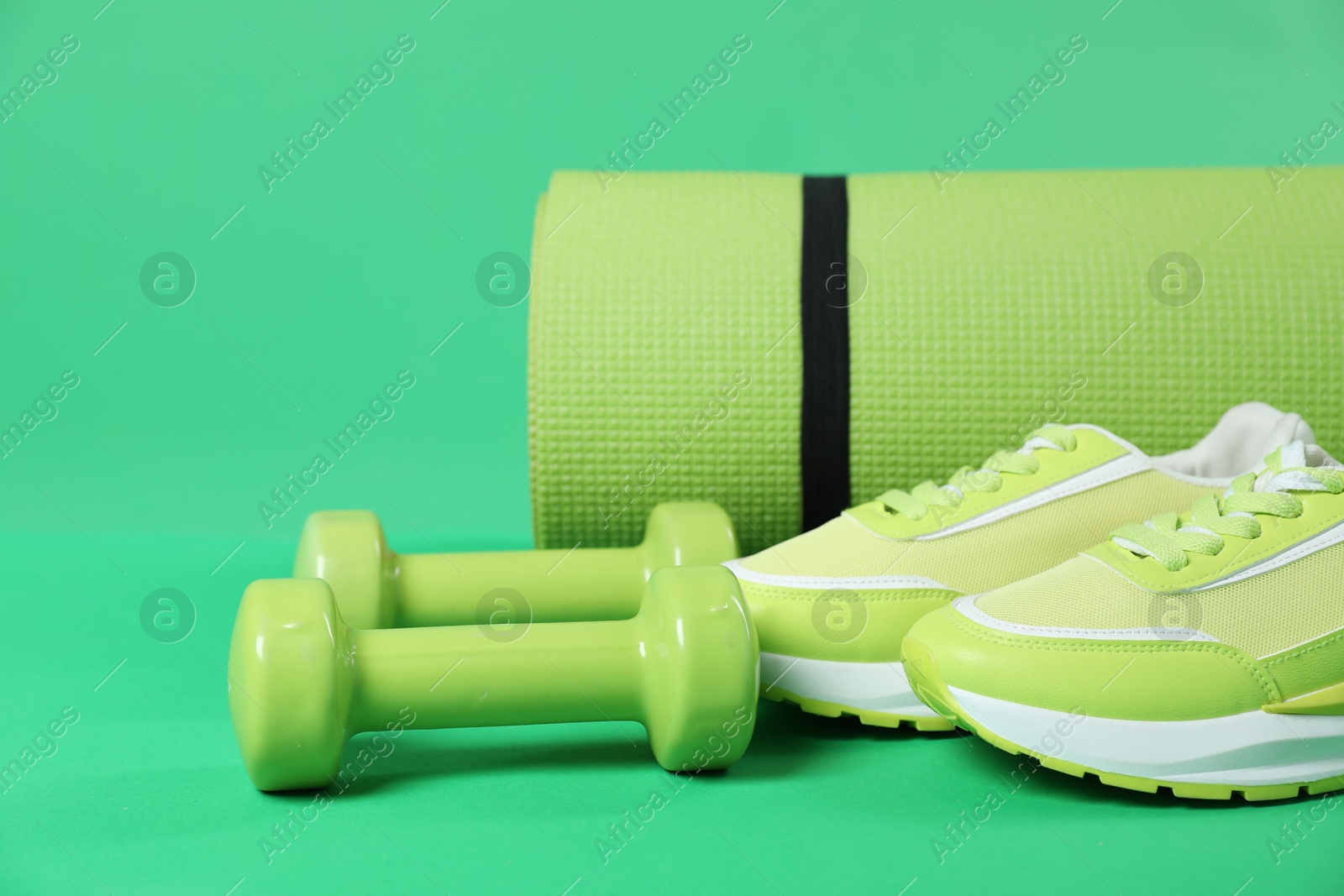 Photo of Fitness mat, sneakers and dumbbells on green background, closeup. Sports equipment