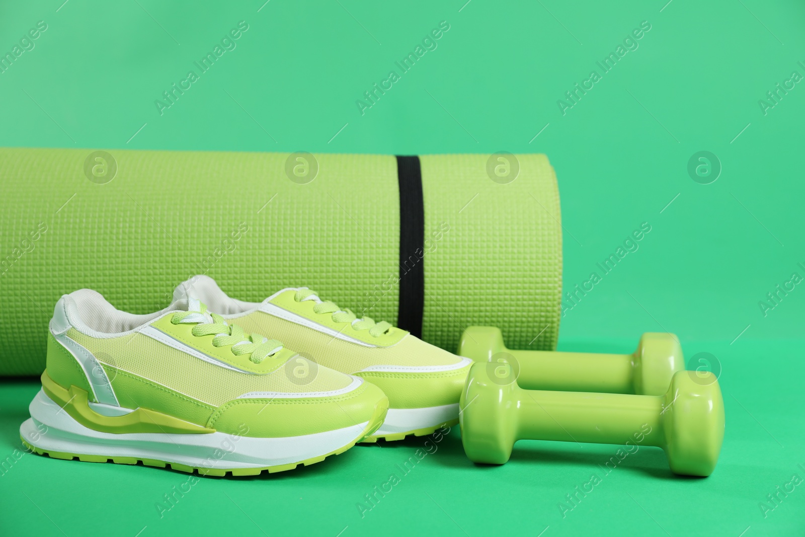 Photo of Fitness mat, sneakers and dumbbells on green background, closeup. Sports equipment