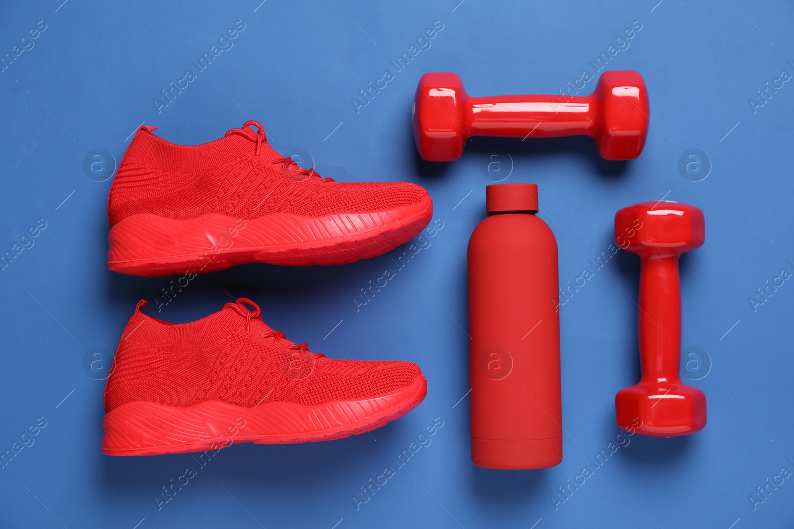 Photo of Sneakers, water bottle and dumbbells on blue background, flat lay. Sports equipment