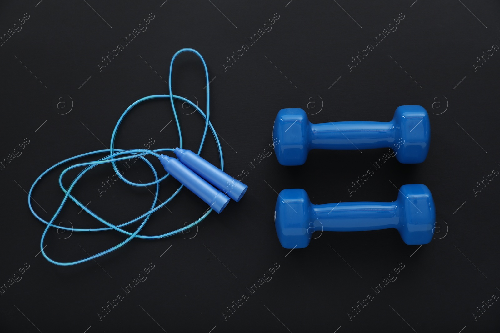 Photo of Dumbbells and skipping rope on black background, flat lay. Sports equipment