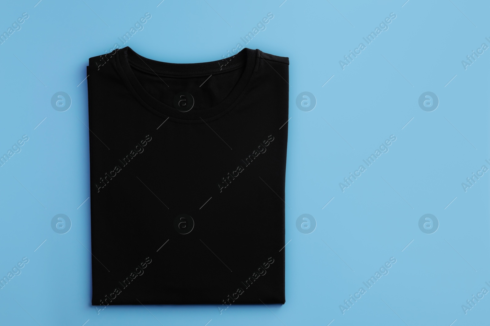 Photo of One blank t-shirt on light blue background, top view. Mockup for design