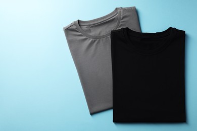 Blank t-shirts on light blue background, flat lay. Mockup for design