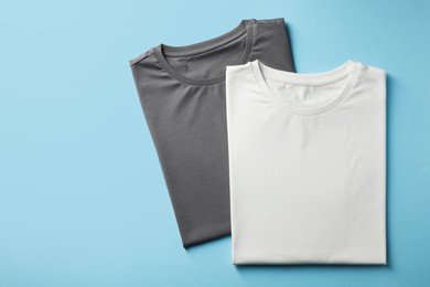 Blank t-shirts on light blue background, flat lay. Mockup for design