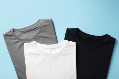 Blank t-shirts on light blue background, flat lay. Mockup for design