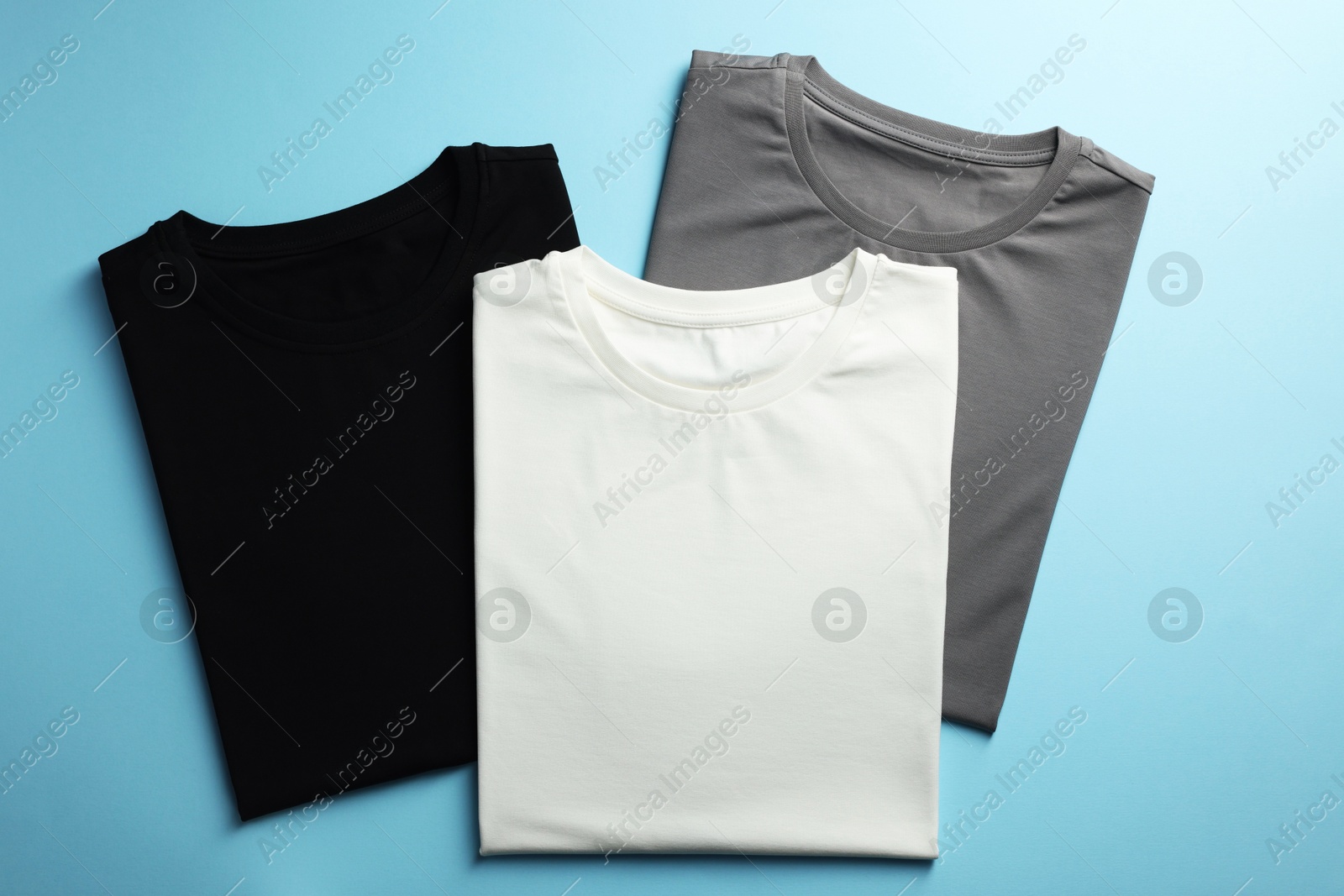 Photo of Blank t-shirts on light blue background, flat lay. Mockup for design