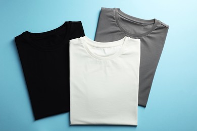 Blank t-shirts on light blue background, flat lay. Mockup for design