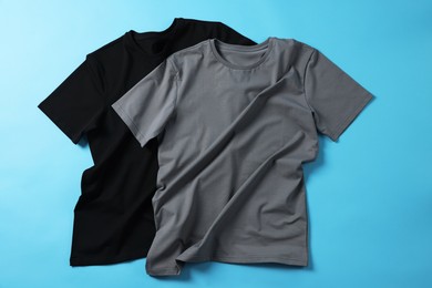 Blank t-shirts on light blue background, flat lay. Mockup for design