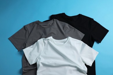 Blank t-shirts on light blue background, flat lay. Mockup for design