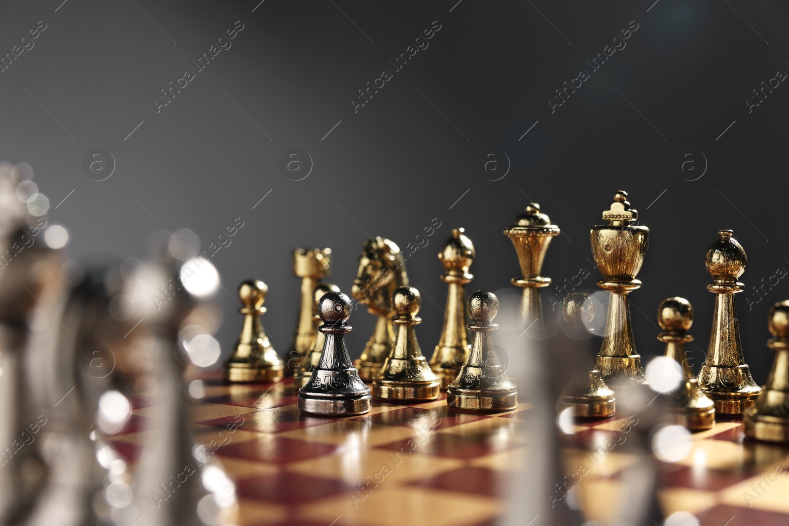 Photo of Silver pawn in front of golden chess pieces on chessboard against grey background, closeup. Competition concept