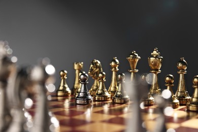 Photo of Silver pawn in front of golden chess pieces on chessboard against grey background, closeup. Competition concept