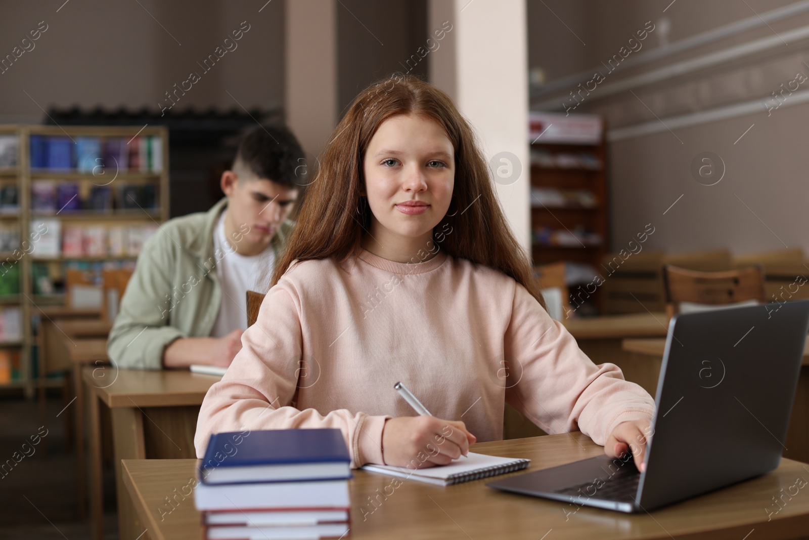 Photo of Girl taking notes while using laptop at wooden desk in public library