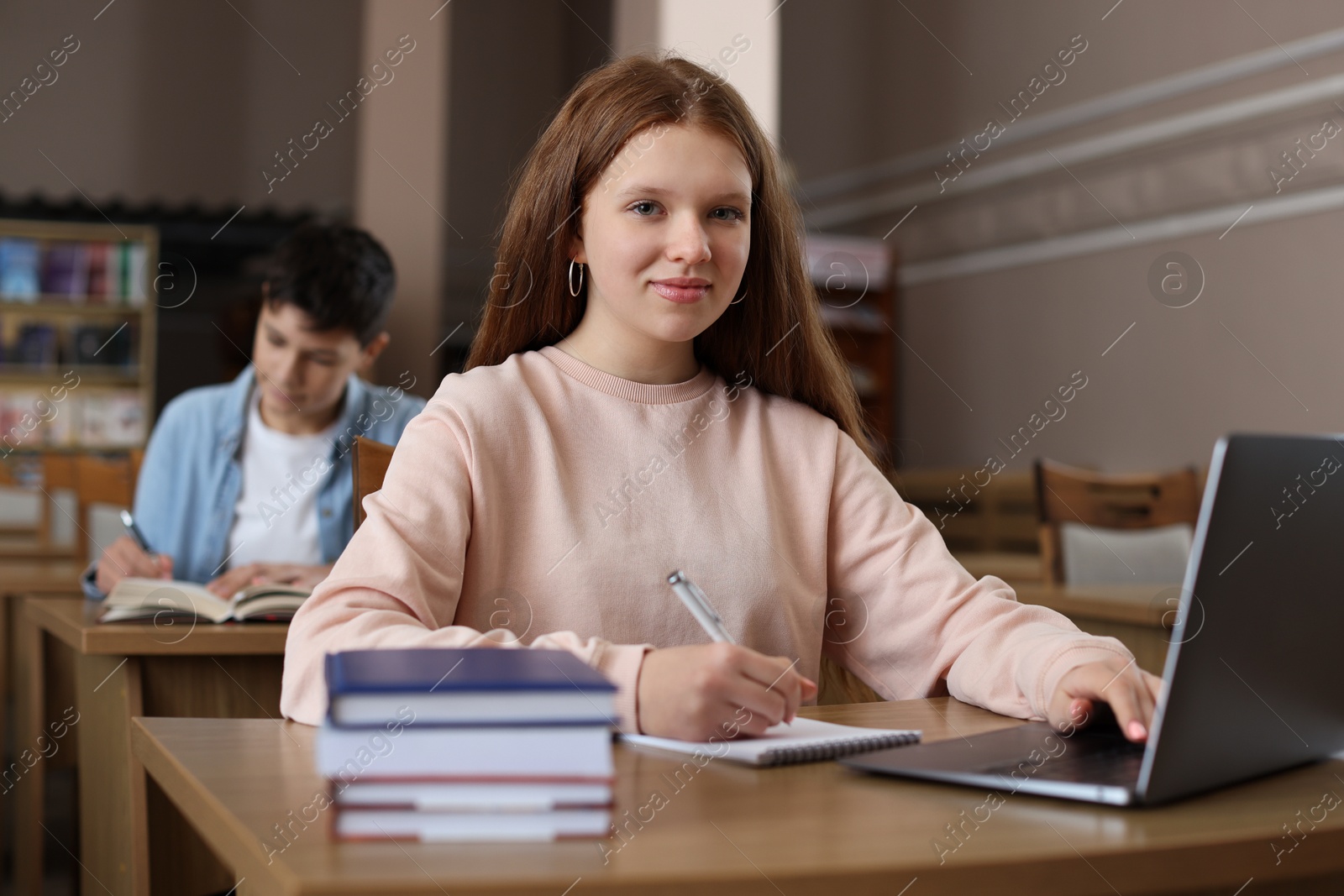 Photo of Girl taking notes while using laptop at wooden desk in public library